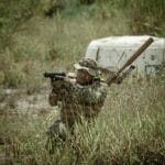 Żołnierz w kamuflażu celuje z broni, ukryty w wysokiej trawie