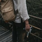 Mężczyzna z plecakiem trzyma drona na drewnianym pomoście wśród traw