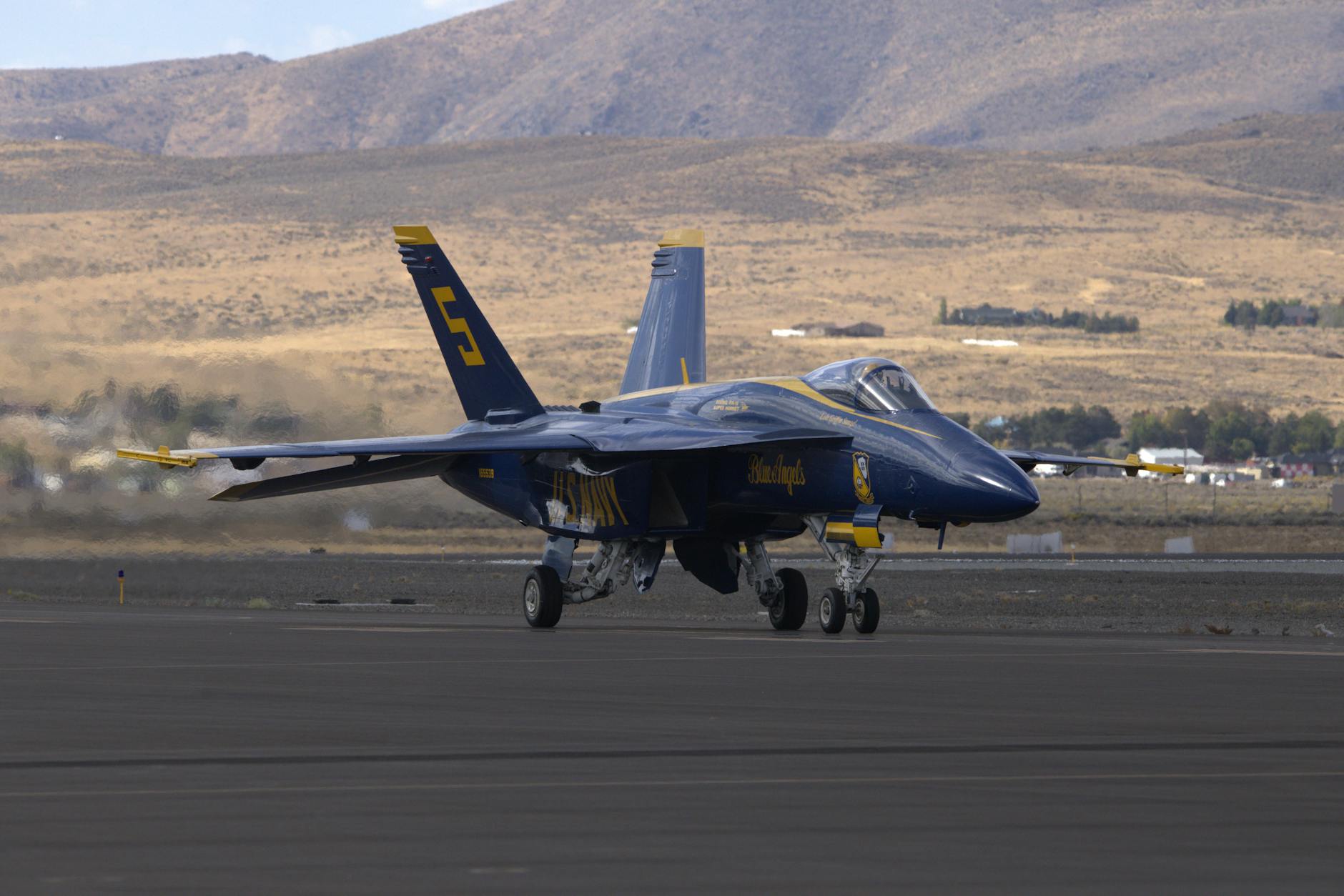 Niebieski myśliwiec kołuje po pasie startowym na tle pustynnych wzgórz