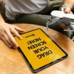 Osoba trzyma używanego drona obok tabletu na drewnianym stole