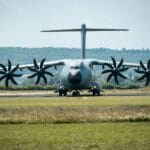 Samolot transportowy A400M z przodu, stojący na pasie przed lasem