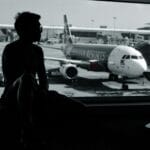 Pasażer w terminalu obserwuje samolot na płycie lotniska