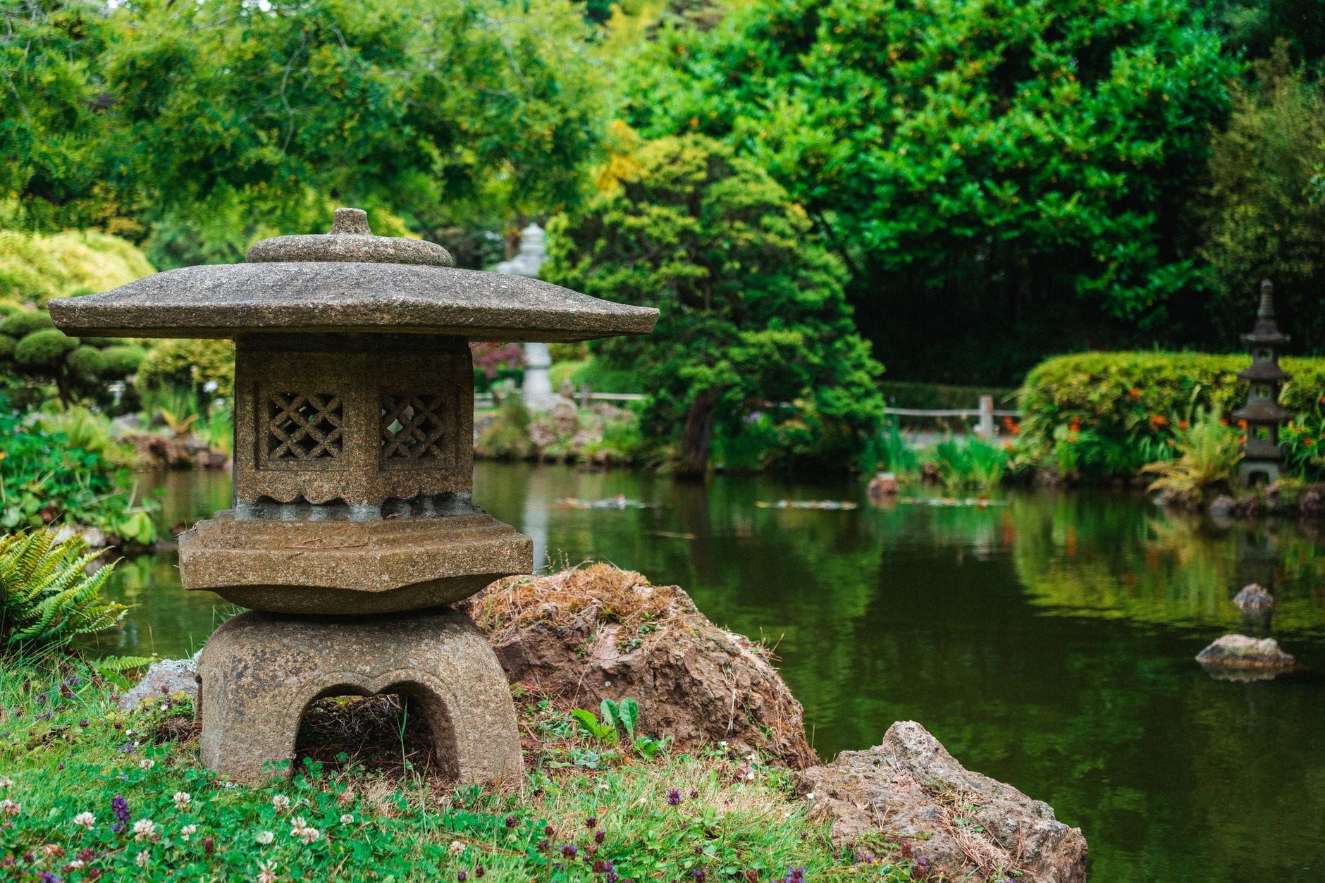 Najpiękniejsze ogrody Japonii nad wodą: przewodnik po miejscach idealnych na spokojny wypoczynek Kamienna latarnia przy stawie w zielonym japońskim ogrodzie